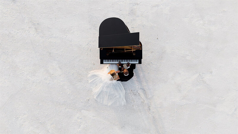 Drone photo from above a couple playing a piano on the salt flats at their wedding.