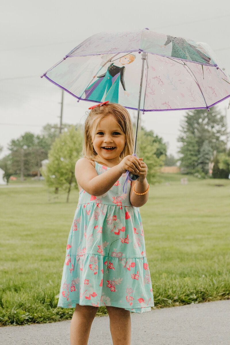 Little girl stands under an umbrella, laughing on a rainy day