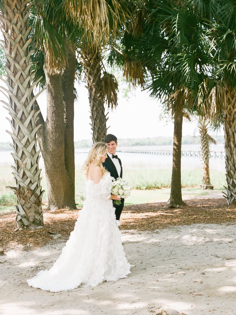 bride and groom walk under palm trees in charleston