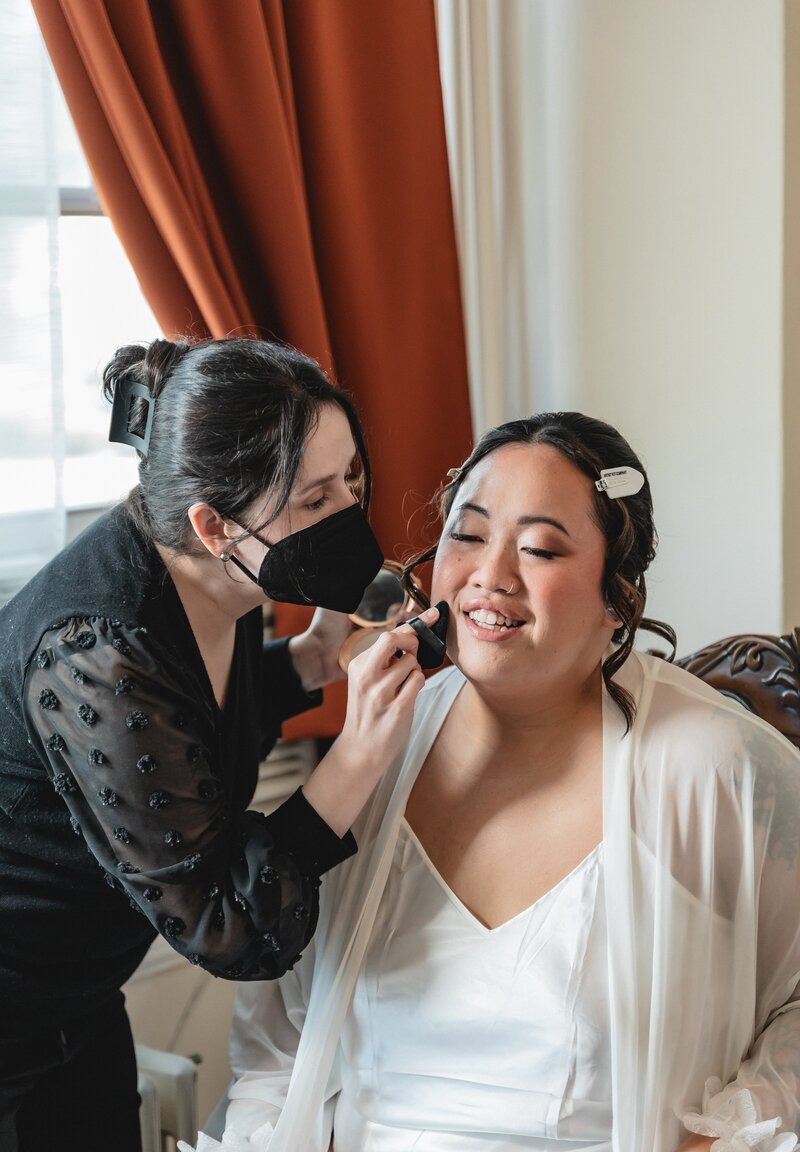 A makeup artist wearing all black applies makeup to a bridal client in Northern Virginia