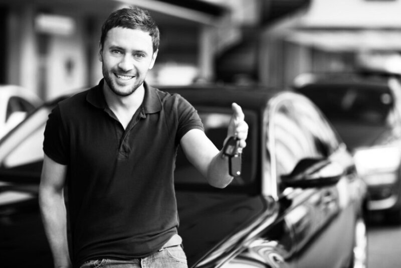 man smiling leaning on his car with car keys