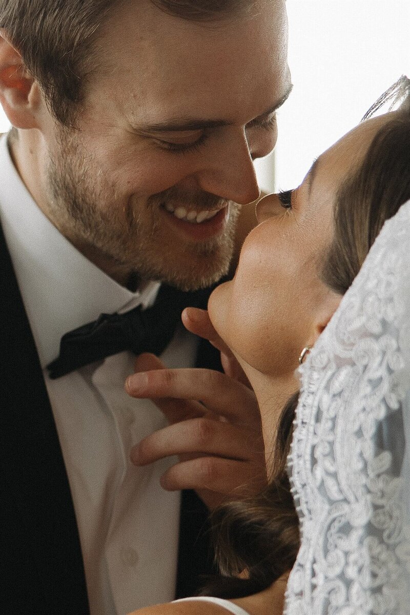 Groom grins at bride and gently cups her face as he goes in for a tender kiss.