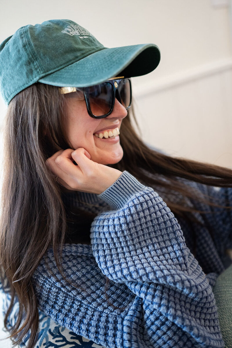 woman gazes right wearing a green baseball cap and large, dark sunglasses