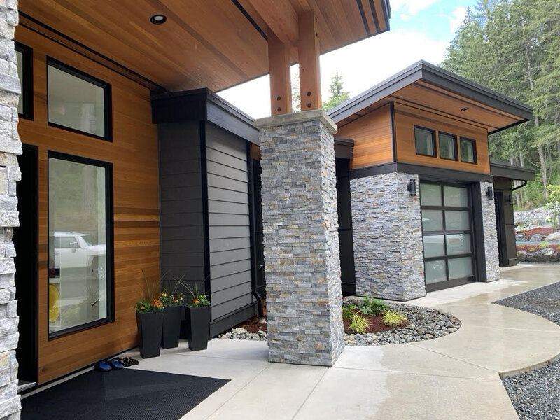 Modern home exterior design with rock pillars, cedar soffits and steel entry door.