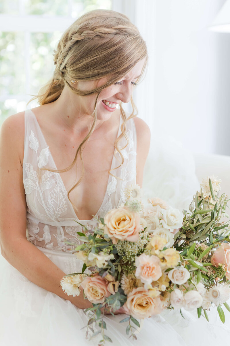 Smiling bride holding a bouquet of peach and white flowers, captured by Destination Wedding Photographer.