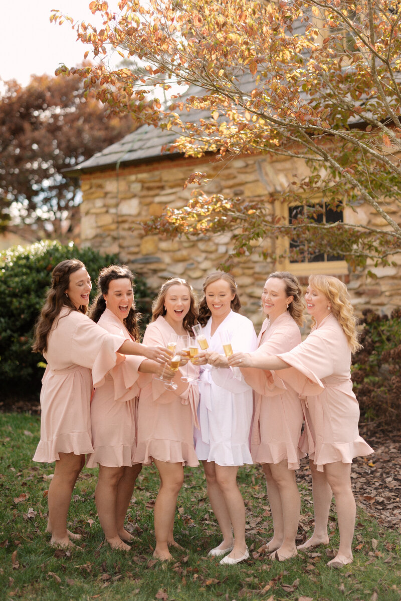 November wedding at Graylyn Estate, designed and planned by Charming Carolina — bride and bridesmaids popping champagne while getting ready with hair and makeup artists in the bridal suite.
