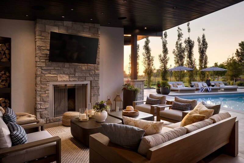 An outdoor living room with outdoor furnishings, stone fireplace with pool side views. 
