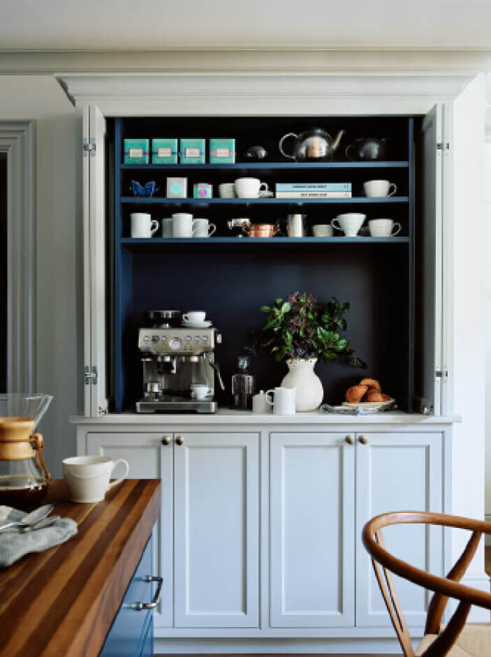 Kitchen designer in Boston maximizes space with a custom coffee pantry featuring light grey cabinets, a navy interior, and storage for an espresso machine and kettle.