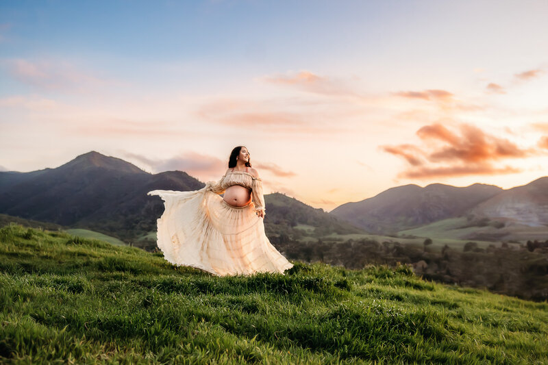 pregnant mom in epic walnut creek hillside. her white maternity gown flows in the wind