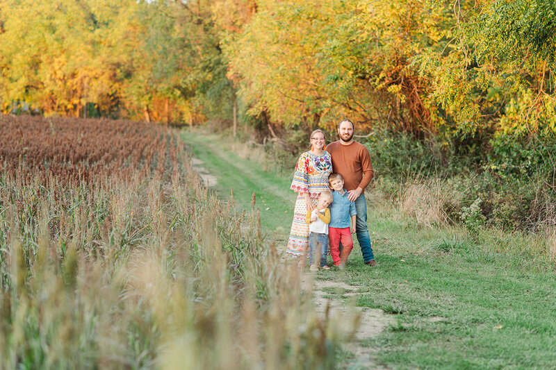 family of four posing together next to a corn field with bright fall colors behind them by lancaster pa photographer