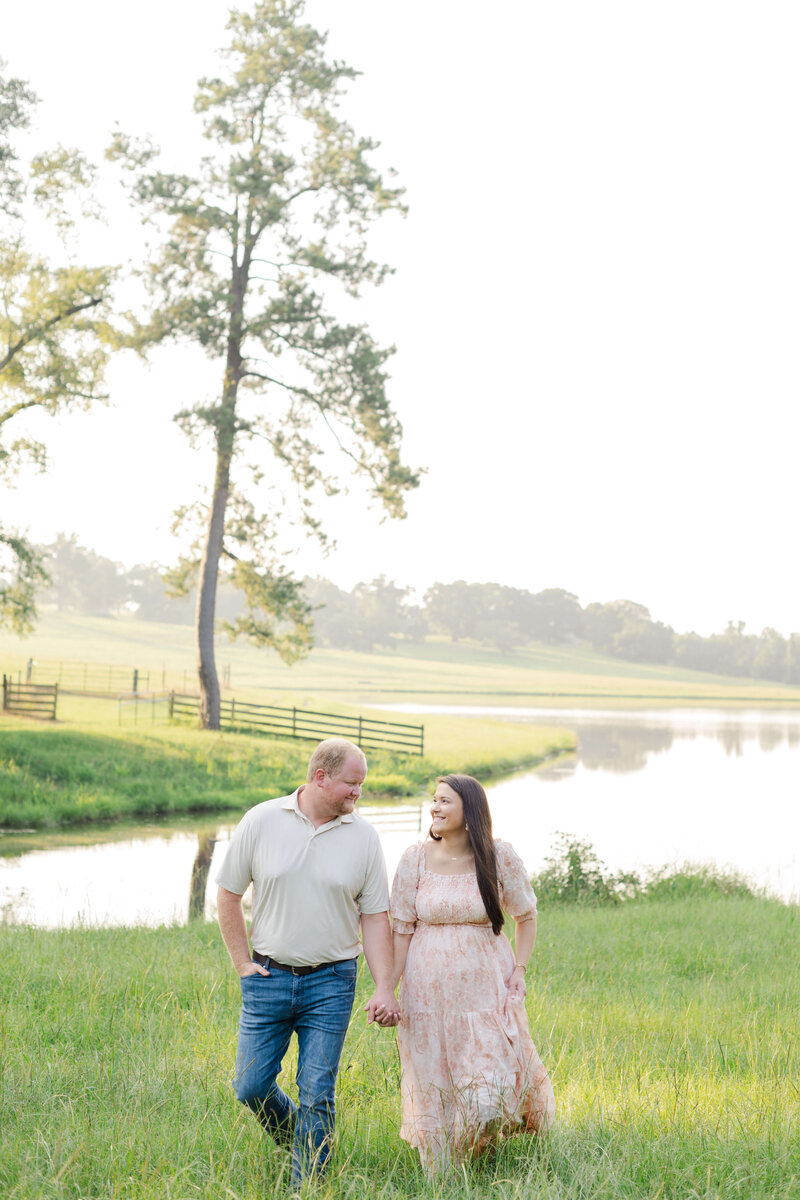 Woman and Man holding hands walking by water for maternity photography session