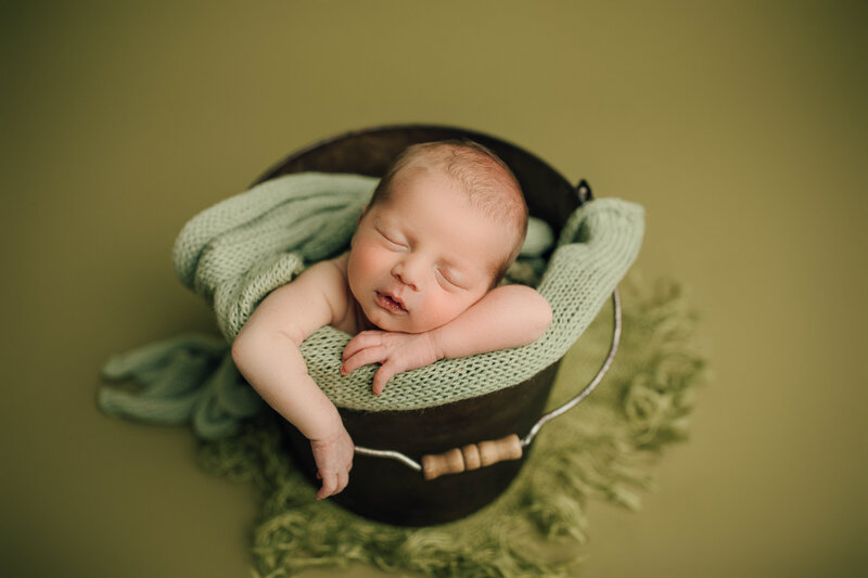 newborn baby in a bucket with a green backdrop