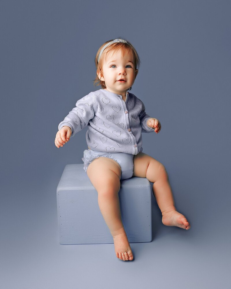 One-year-old baby sitting on bold colored backdrop in Austin milestone studio
