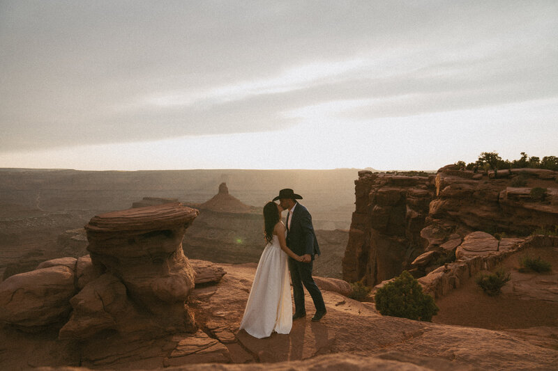 Couple kissing on the edge of a cliff at sunset with the canyon in the background 