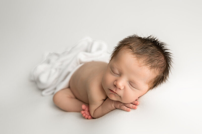 newborn in sleeping pose on cream backdrop with headband and white outfit