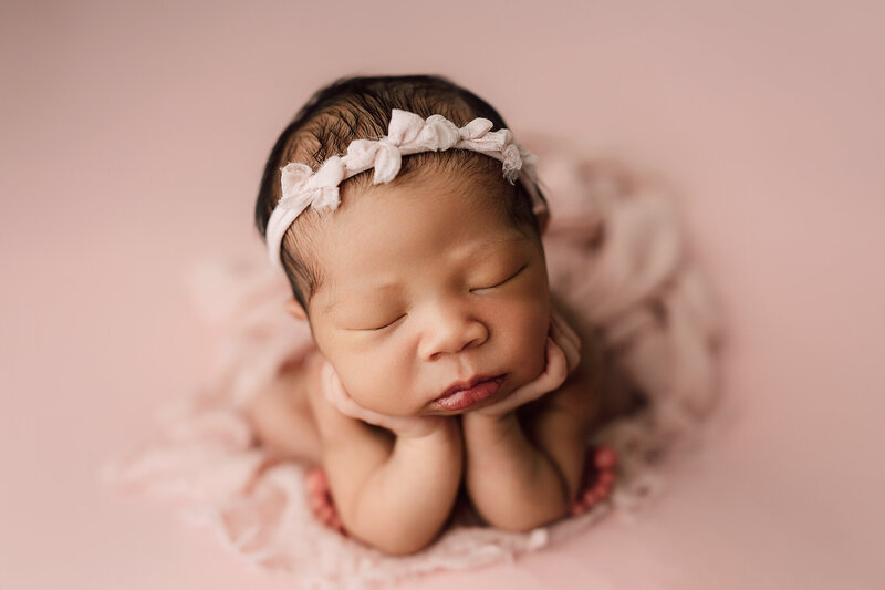 Baby girl with her head in her hands on a pink blanket