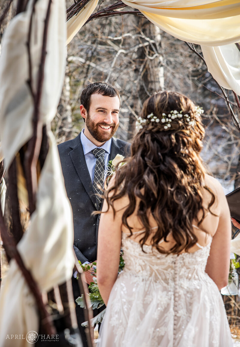 Groom Smiles at his Bride During Wedding Ceremony Outside at Romantic Riversong Inn Estes Park CO