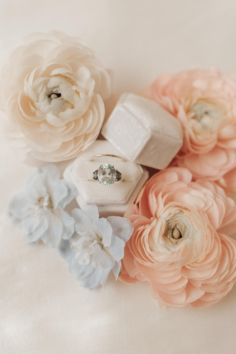 Engagement ring amidst pastel flowers.