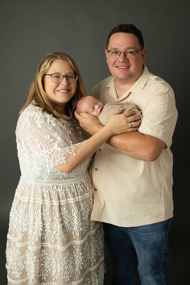 mom in a floral dress and dad in a green henley holding their newborn boy with their eyes closed