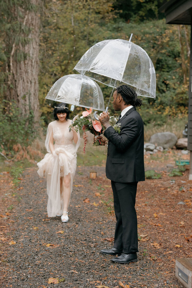 Bride and groom walking holding a clear umbrella