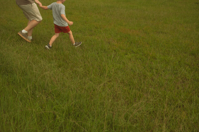 A father and son hold hands and run down a grassy hill at Noonday Creek Trail. 