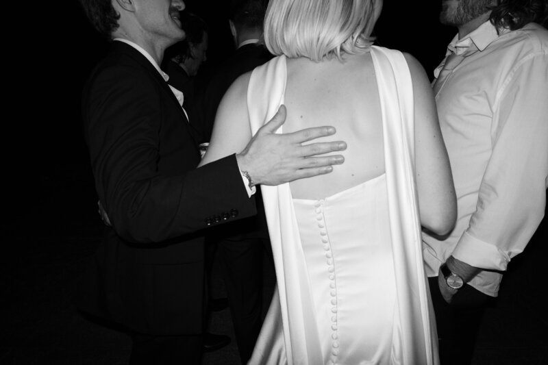 Black and white candid of bride in satin gown with button detail during lively wedding reception