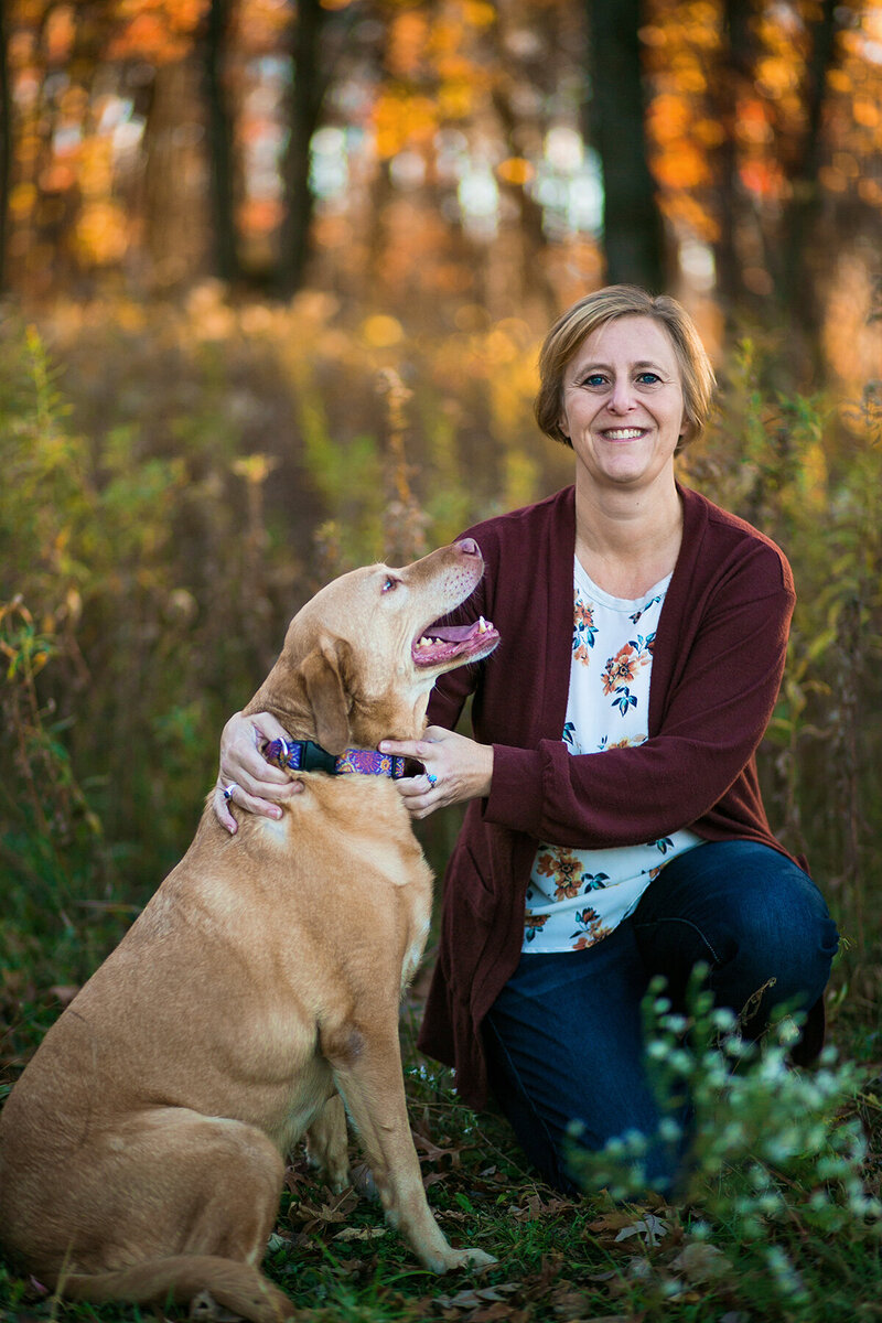 Woman sitting in a field with a yellow lab looking up at her.