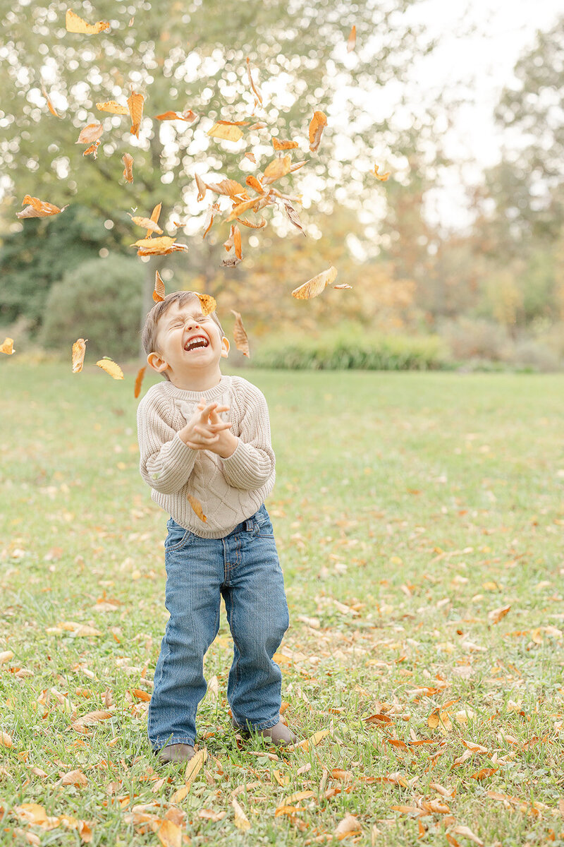 golden leaves falling as he laughs during Alexandria, Virginia fall minis