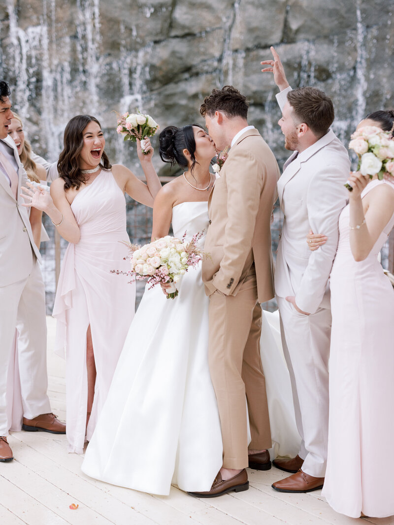A bride and groom kissing while their wedding parties celebrate around them