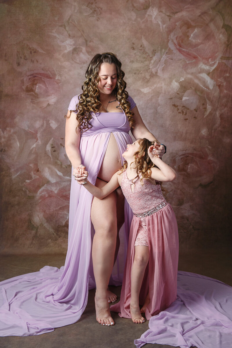 Professional portrait of a pregnant woman and her young daught looking at each other on a brown floral background
