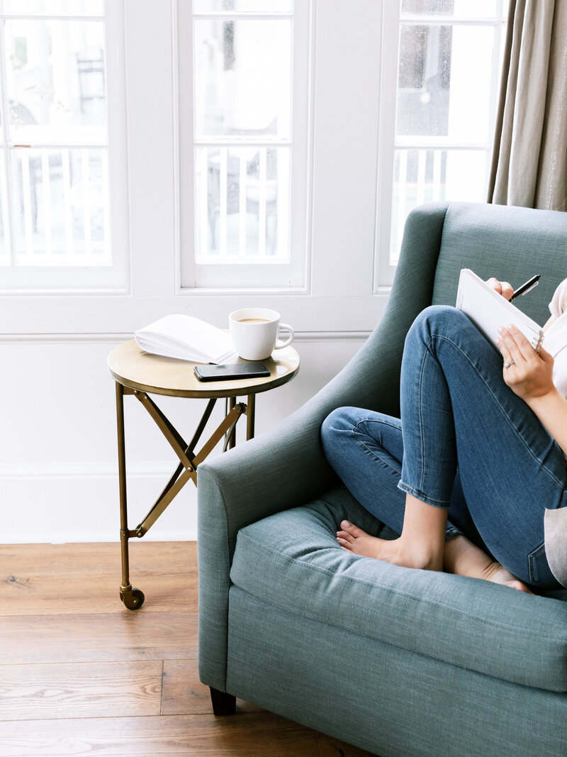Woman sitting curled up in a blue chair writing in a notebook