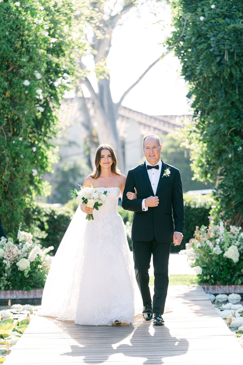 dad wearing a traditional black tux walking his daughter down the aisle daughter is wearing a custom Monique Lhuillier wedding dress at the Belmond El Encanto in Santa Barbara CA captured by Santa Barbara wedding photographer Magnolia West Photography