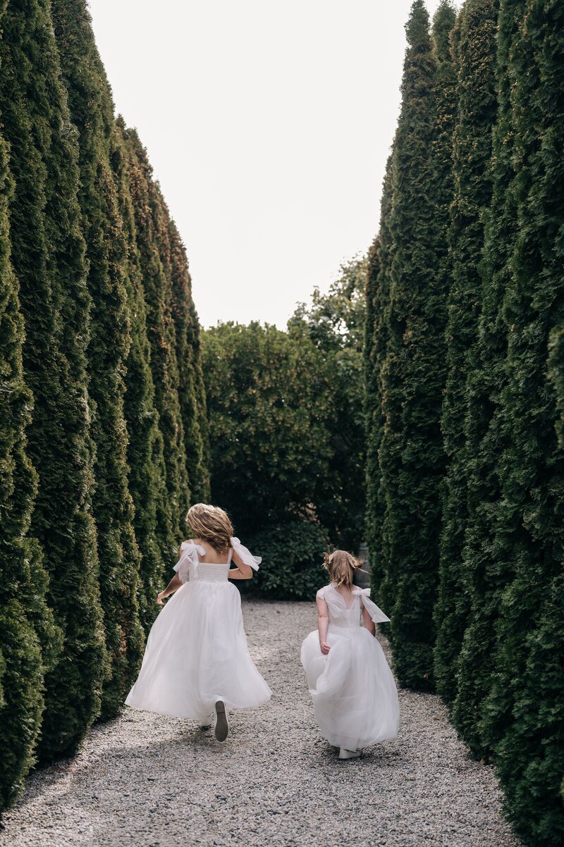 two flower girls run down the tree-lined path at the winehouse wedding venue in queenstown