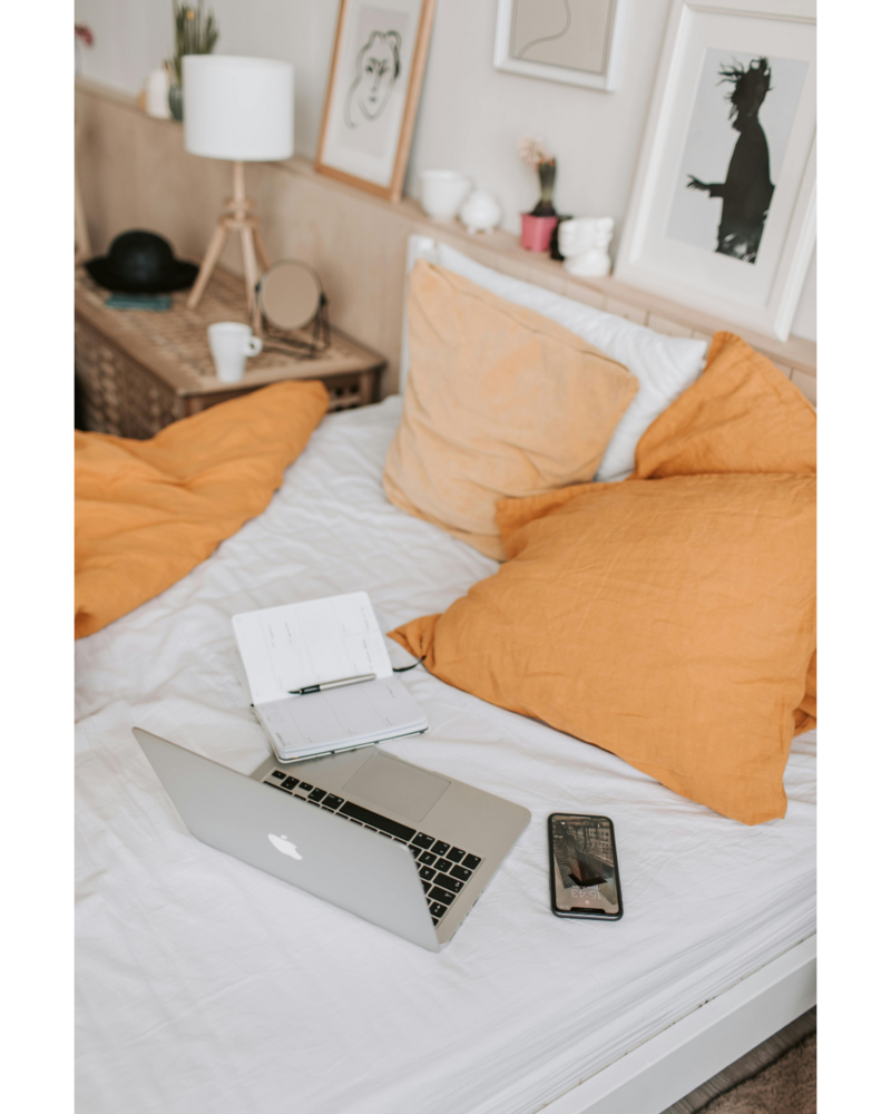 Laptop and notebook on bed