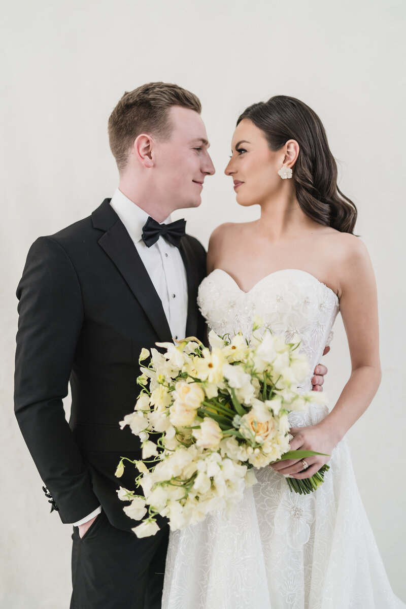 Bride and groom standing in studio lighting with classic style and floral bouquet—elevated, poised, and emotionally present.