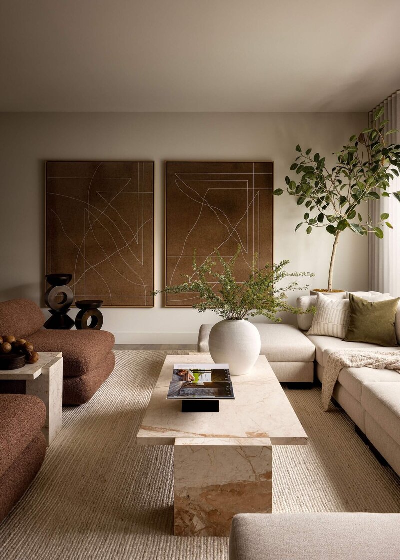 Japandi-inspired living room featuring natural marble coffee table, statement rust artwork, and oversized burgundy chairs for a warm, minimalist aesthetic.