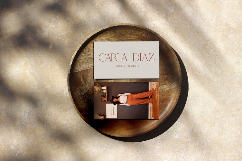 Two business cards lie on a round wooden plate. The card on top reads "CARLA DIAZ Hair &amp; Health," and the card below shows a woman standing next to a counter, perfectly capturing the essence of our websites for salons.