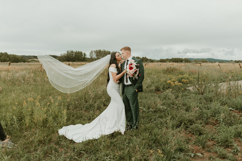 Ashton Idaho bridal shoot with long flowing veil and groom in an emerald green suit. Field of green grass and flowers. 