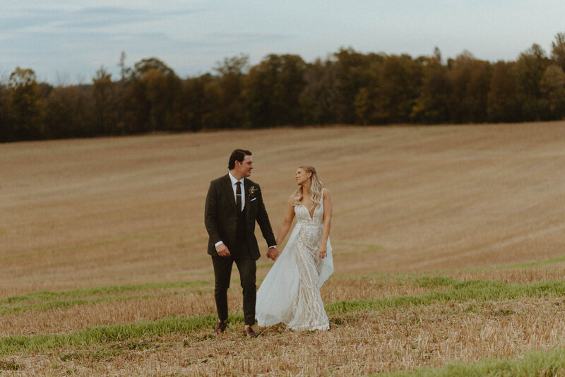 bride and groom walking through golden field