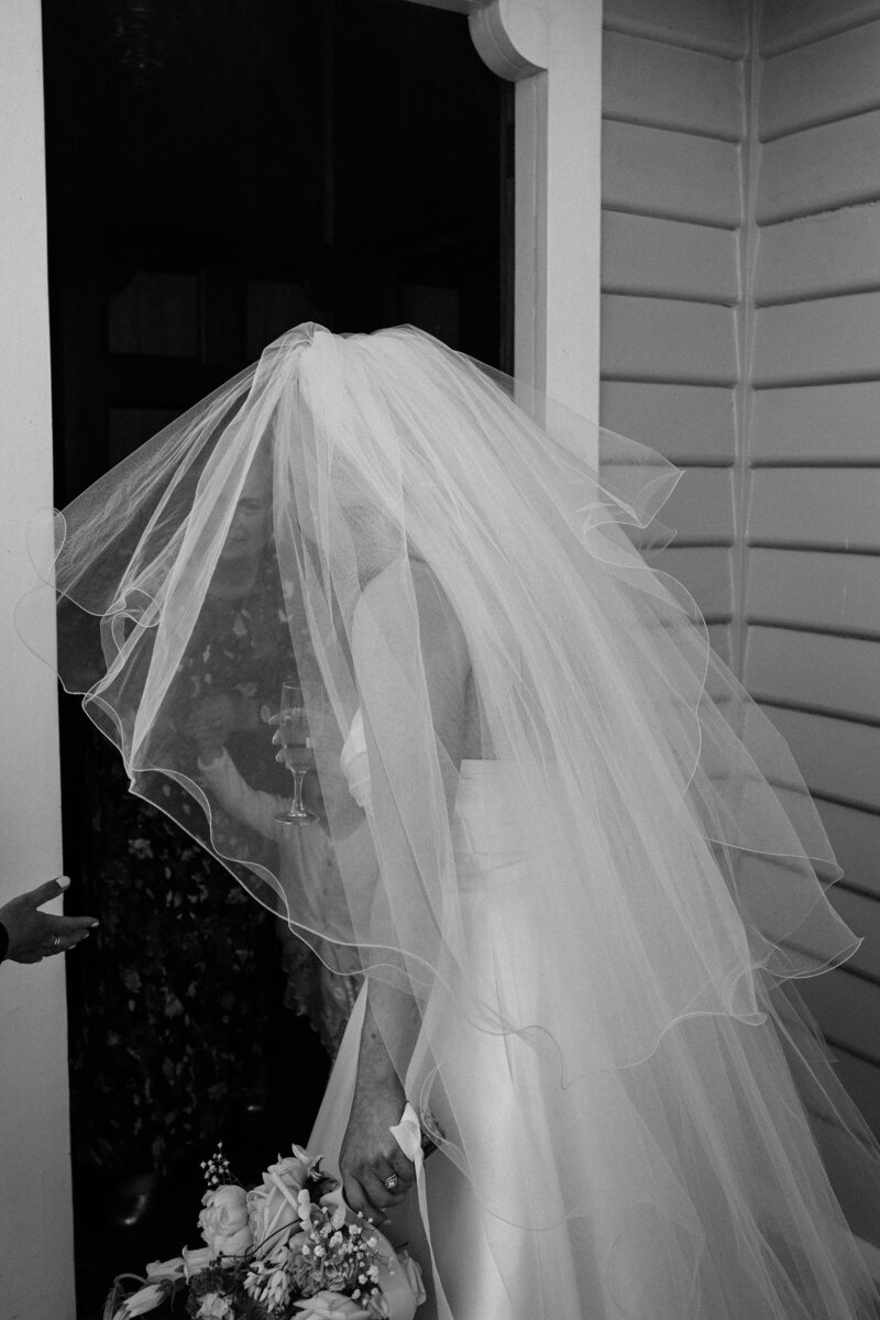 black and white photo of a bride with a veil going through wooden church door at farm chapel near gore