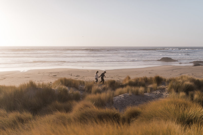 man and woman walking through dunes to ocean