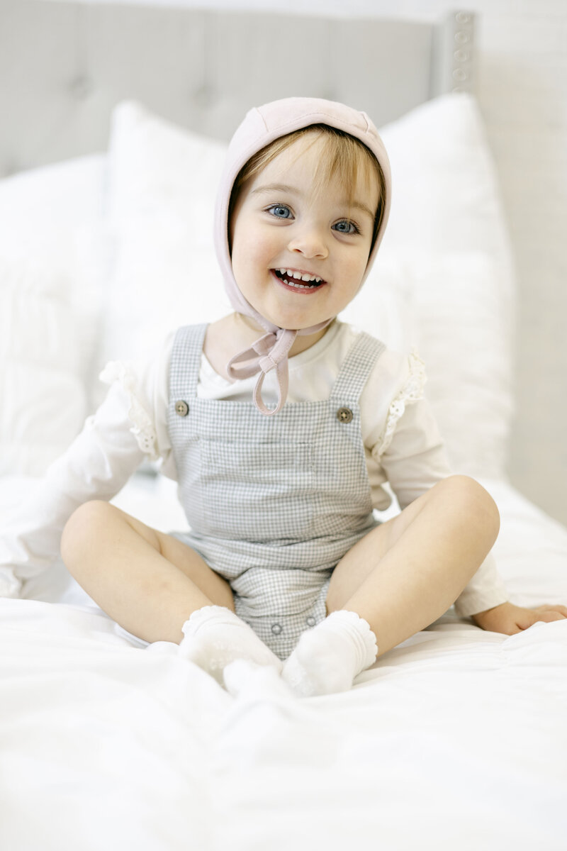 Little girl styled by Kathleen Jablonski Photography sitting on a bed in studio