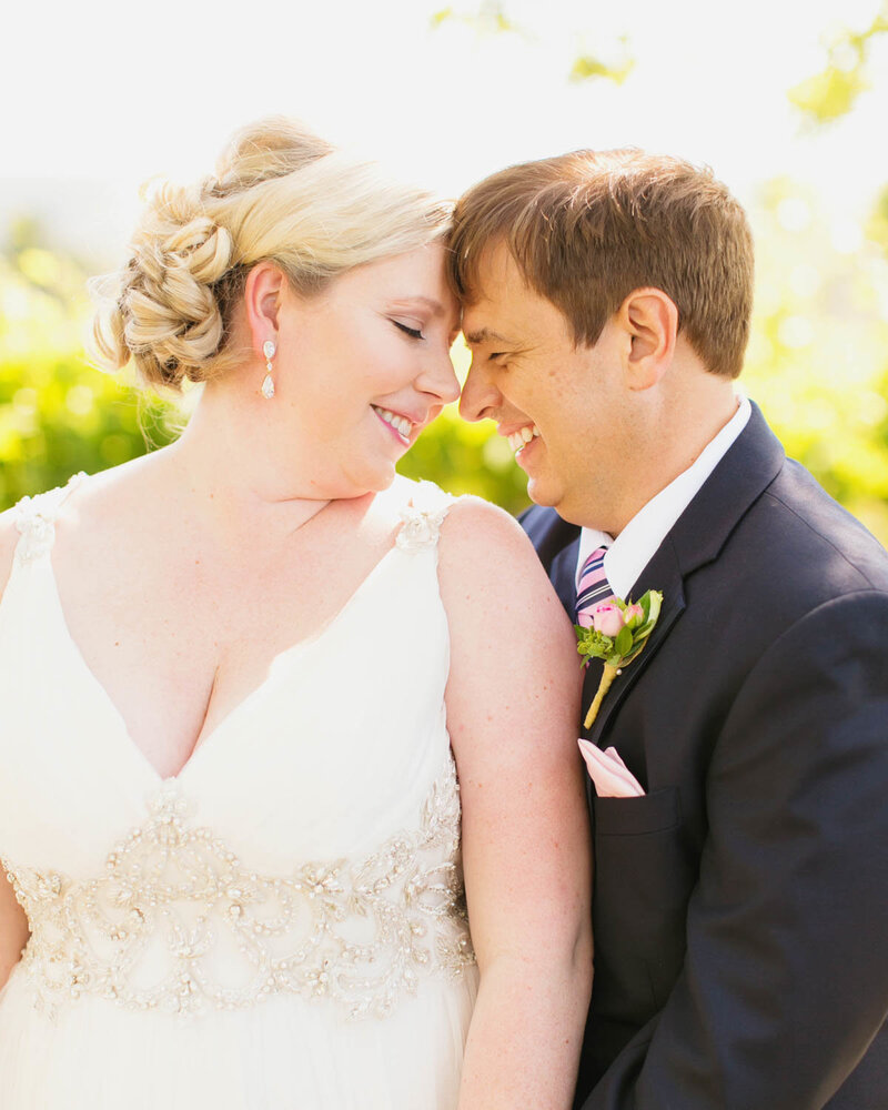 Groom stands behind Bride as they both lean into each other touching noses and foreheads