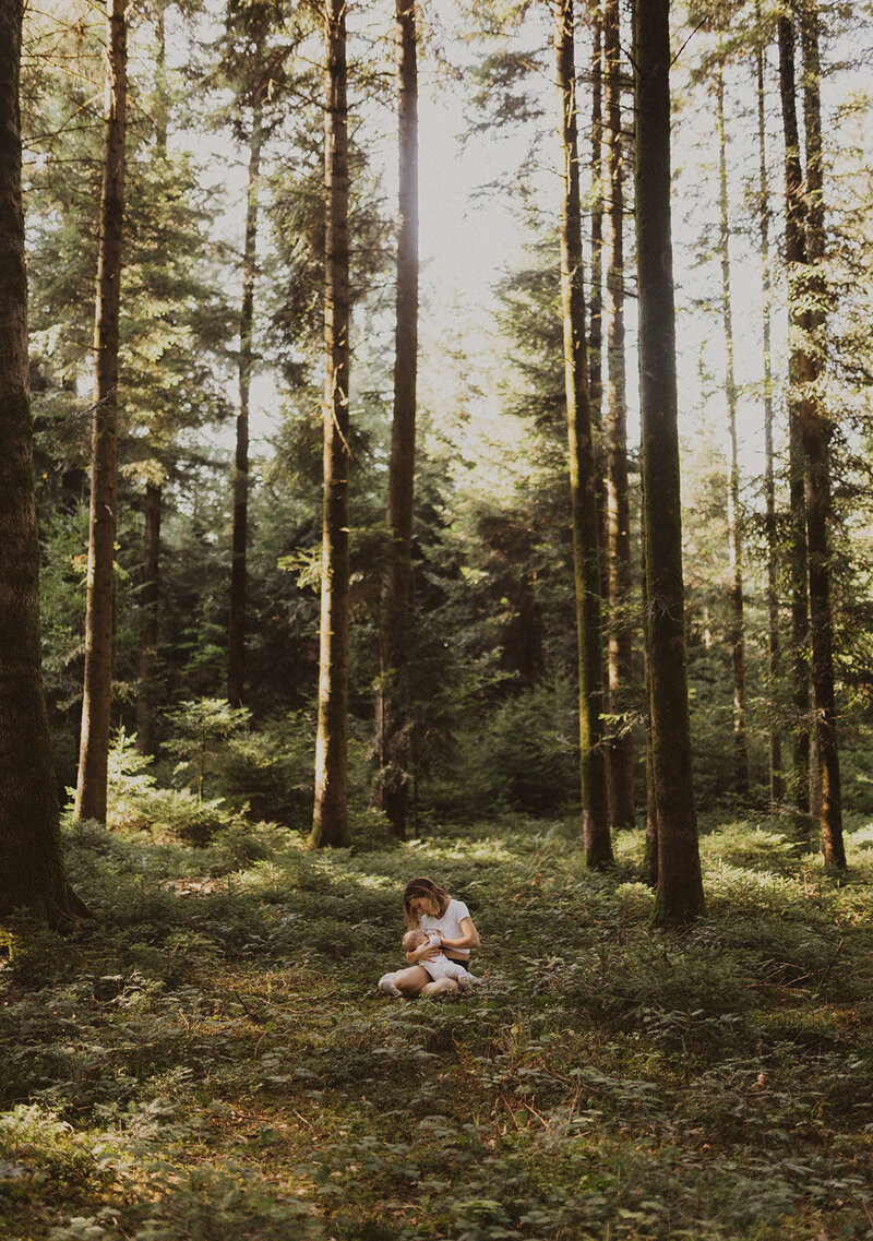 Eine Frau stillt im Wald ihr Baby.
