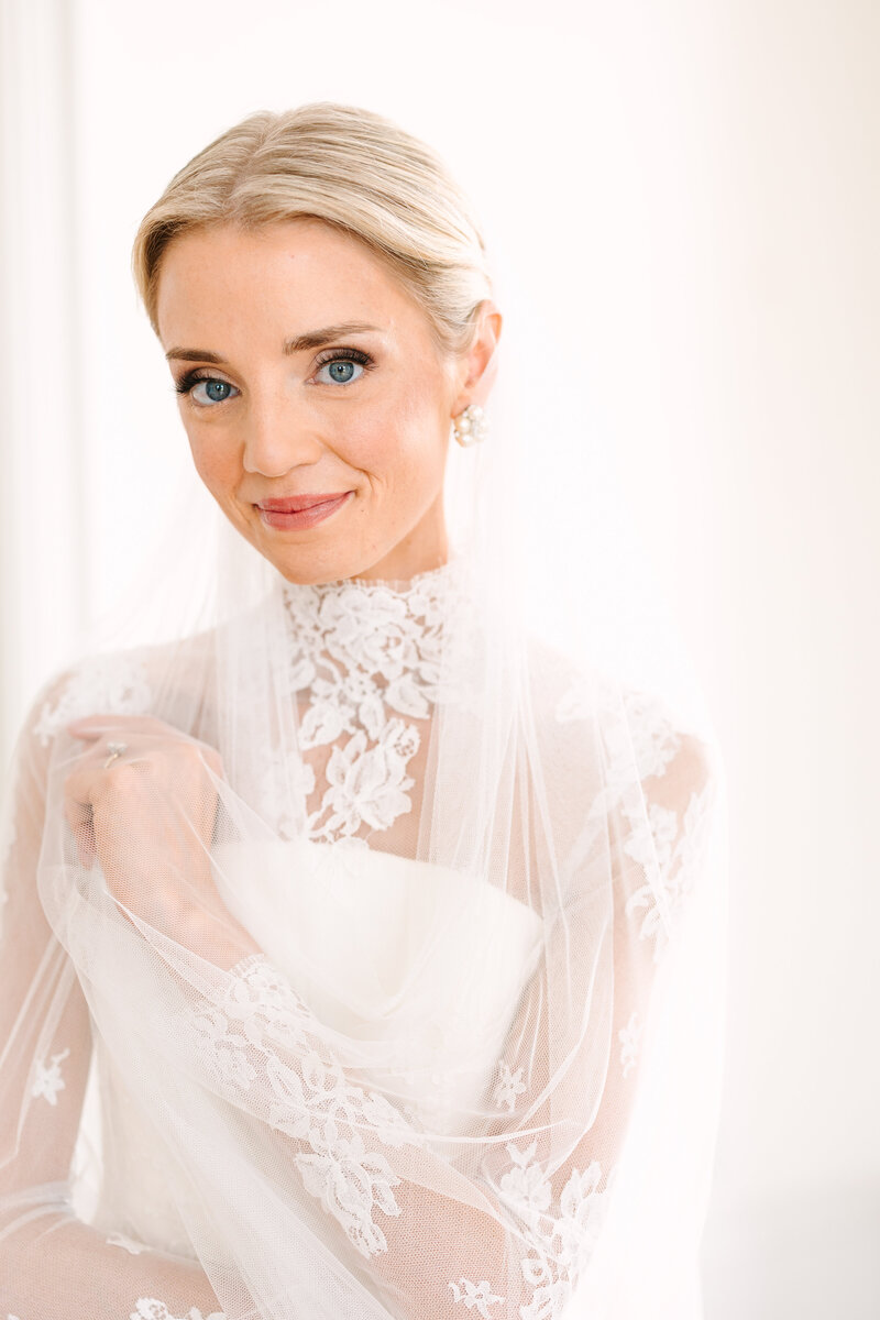 Close up portrait of bride soft smiling at the camera holding onto her veil