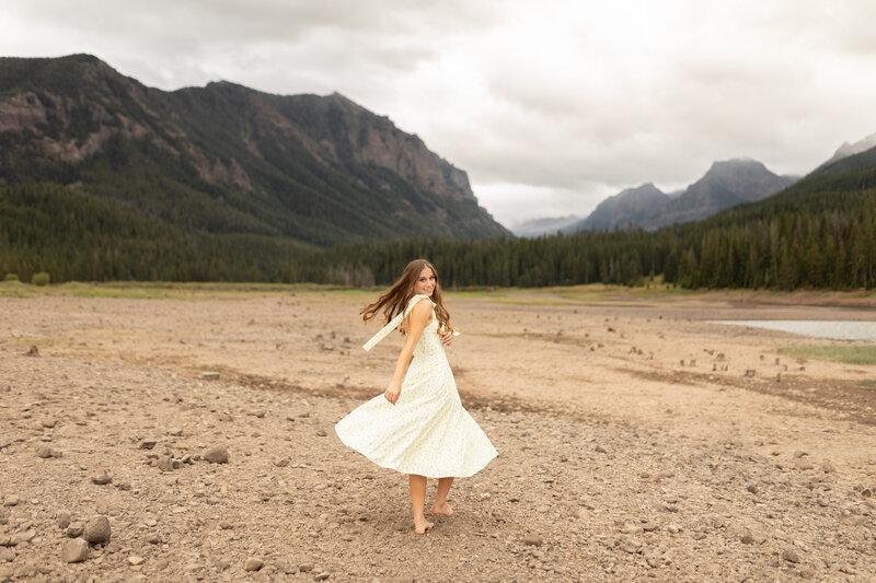 Twirling in front of mountains a young woman smiles.