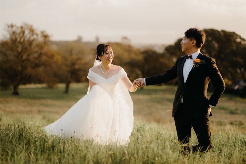 A bride and groom walking in a field during their photoshoot on their wedding day with auckland photographer Tashina Narelle