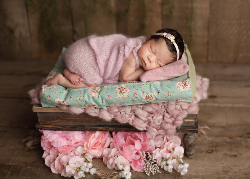 newborn girl on a mattress in a pink knit romper
