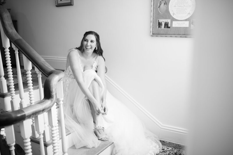 Black and white photo of bride putting on her shoes on a staircase, captured during a Williamsburg wedding planned by Sweet Caroline Events