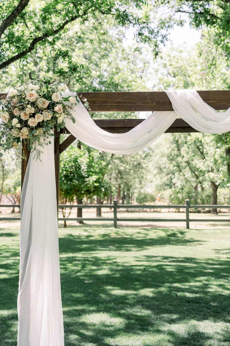 Gorgeous rustic wedding arch decorated with ivory draping and floral piece, captured by Tony George Photography